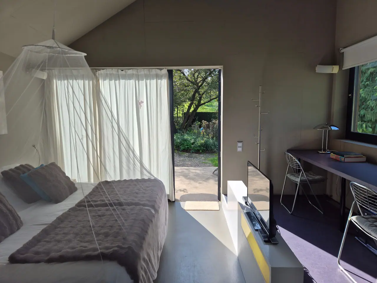 Lichte slaapkamer met tweepersoonsbed onder een klamboe en een open tuindeur