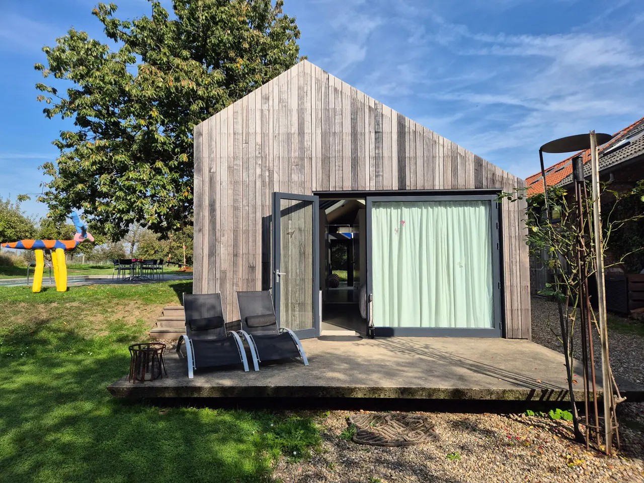 De houten voorgevel met open tuindeur en twee ligstoelen op het voorterras