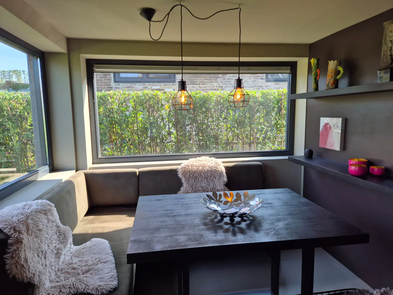 Eethoek met bank, donkere tafel en twee hanglampen voor een groot raam