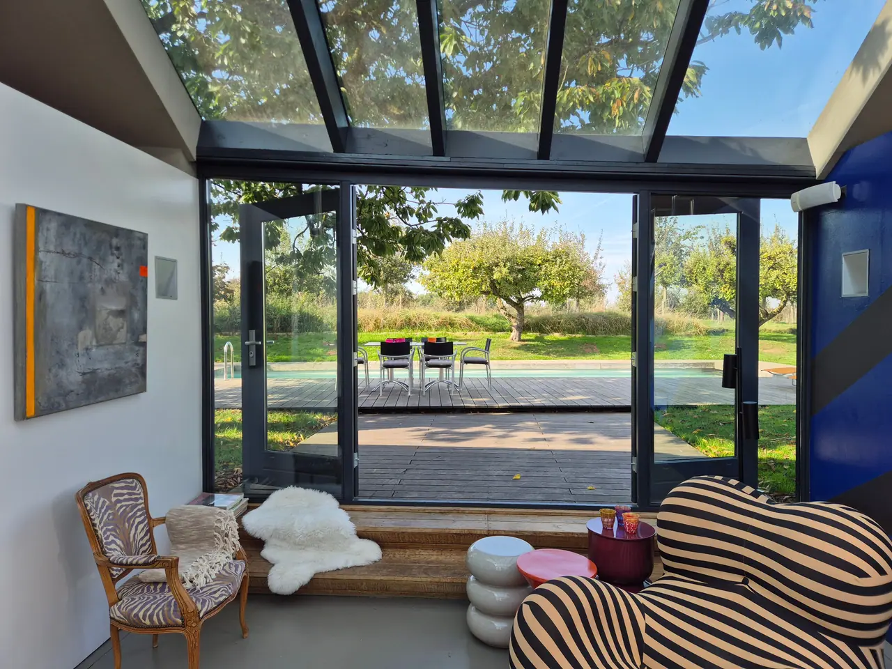 Vanuit de woonkamer door de open glazen deuren naar het terras, zwembad en de boomgaard