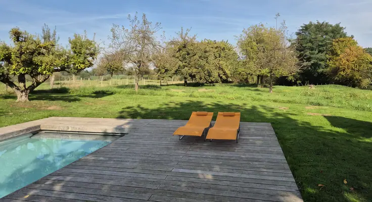 Twee oranje ligbedden op het terras met uitzicht over de boomgaard en de wei