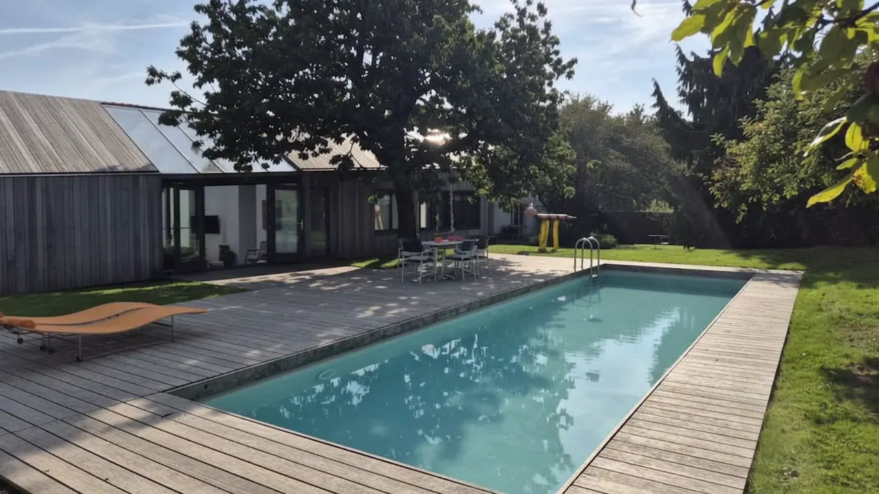 Het 12 meter-zwembad met houten terras, oranje ligbedden en het houten huis met glazen dak